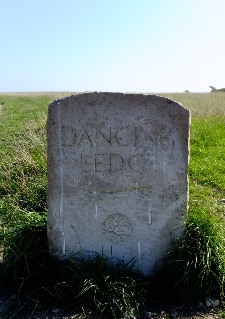 A stone waymarker sign pointing to Dancing Ledge on the South West Coast Path, Isle of Purbeck, Dorset, UK