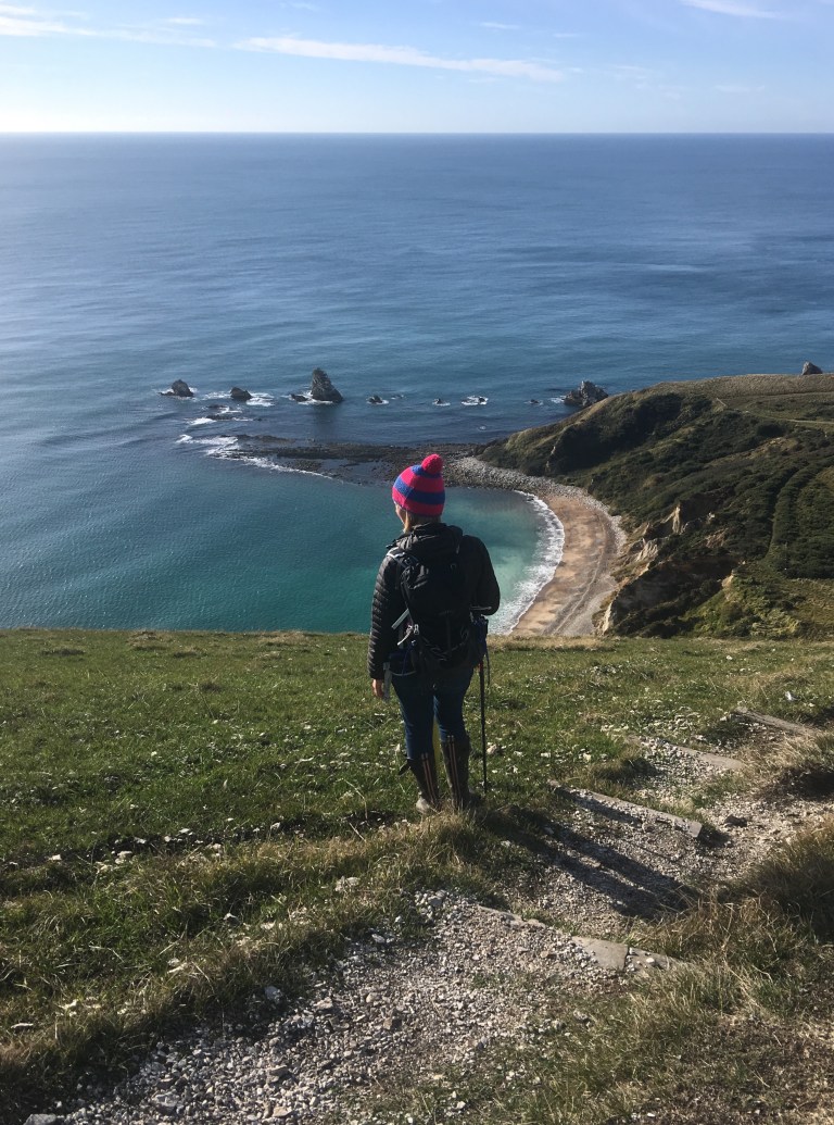 A woman on the South West Coast Path looking town on Mupe Bay and the sea, on the Jurassic Coast, Dorset