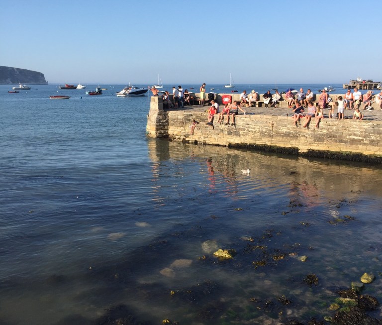 Tourists sitting on the quay in the sunshine at Swanage, Dorset