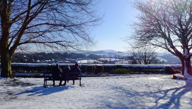 People sitting on a bench in the winter sun on snow covered Park Walk, Shaftesbury 